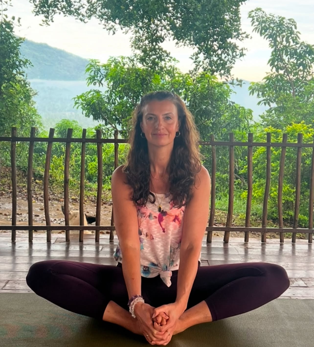Yoga instructor Alice sits smiling in butterfly pose with natural background