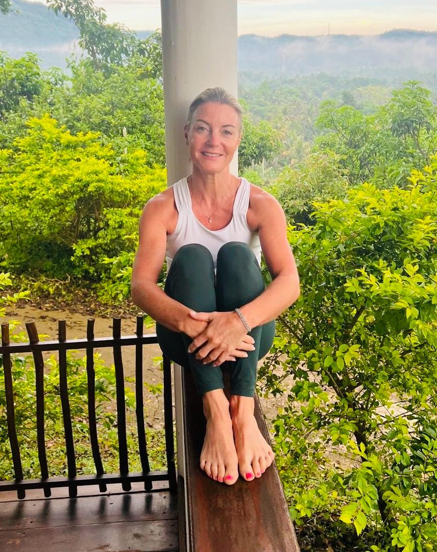 Pilates instructor Michelle sits along balcony railing with stunning green scenic background